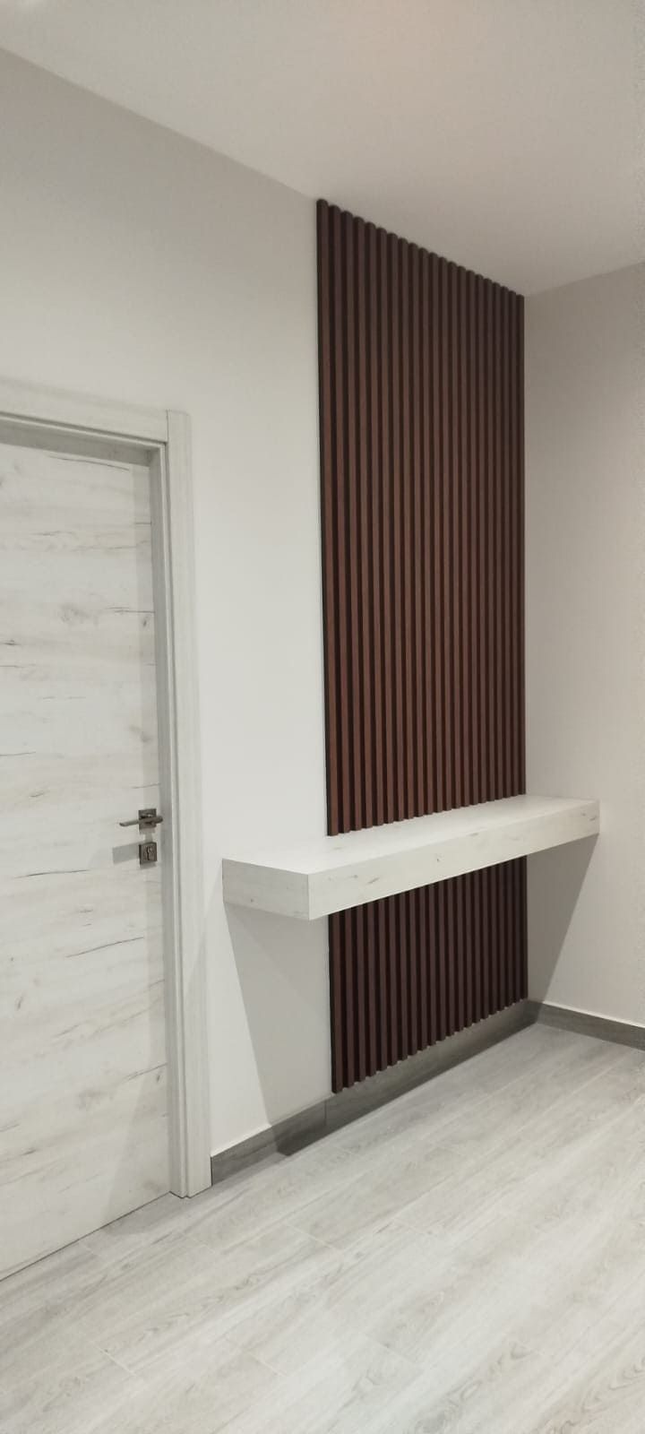 Un pasillo moderno con una pared decorativa con paneles de madera y una mesa consola flotante blanca.