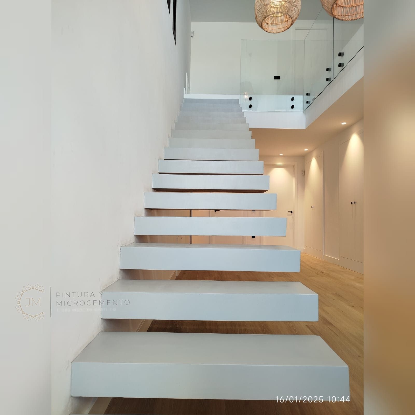 Moderna escalera flotante de color gris claro sobre una pared blanca que conduce a un segundo nivel.