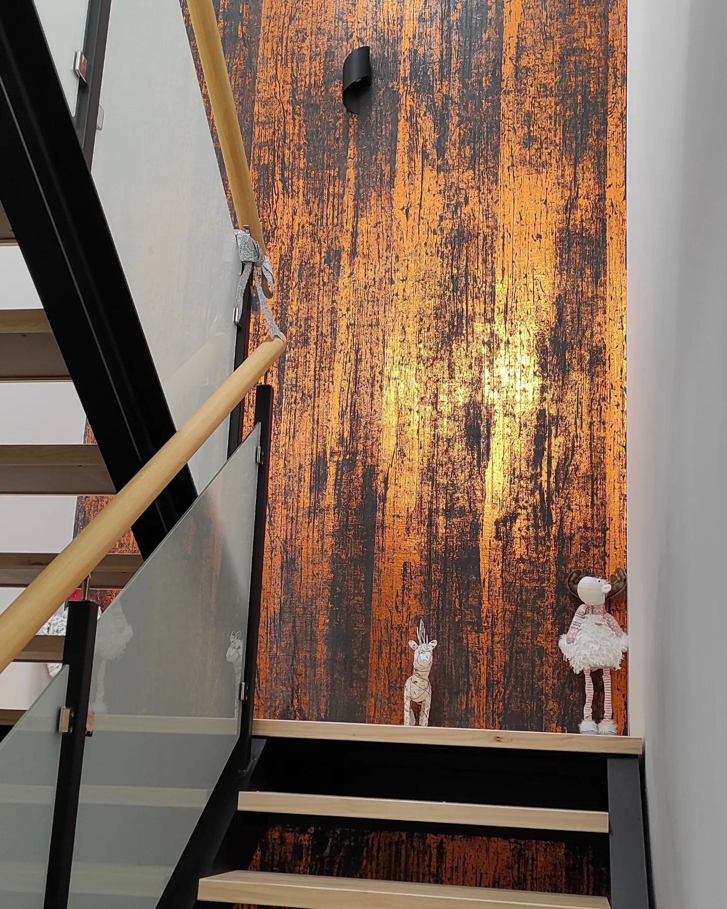Escalera junto a una pared metálica de color óxido con pasamanos negro y una pequeña lámpara de pared blanca.