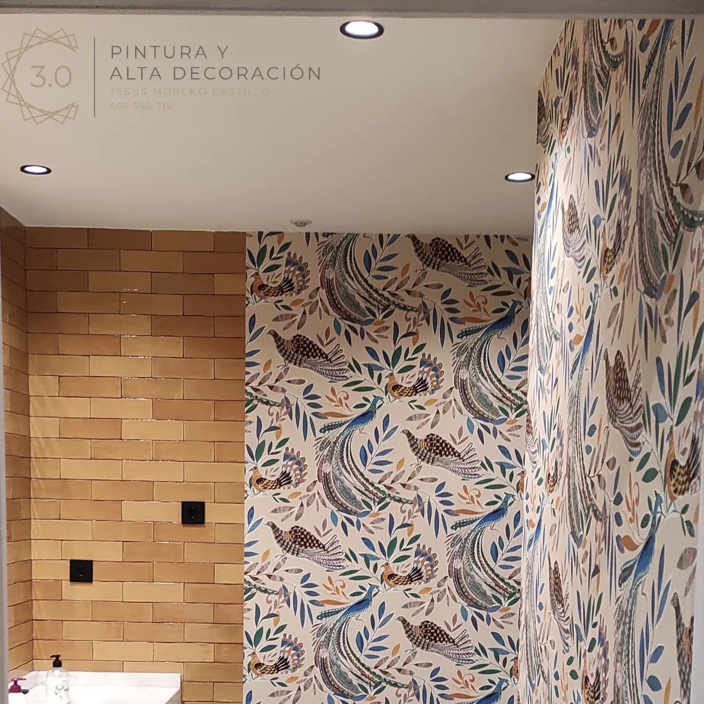Papel pintado decorativo con motivos florales en un pasillo con una pared de ladrillo visto y luces empotradas en el techo.