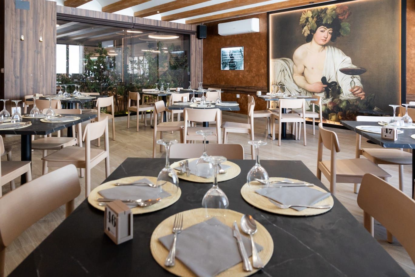 Interior de restaurante moderno con mesas puestas, sillas de madera y un gran retrato en la pared.