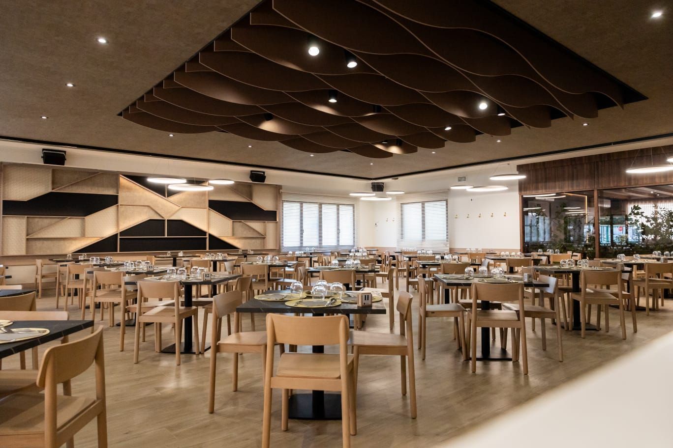 Cafetería moderna vacía con filas de mesas y sillas de madera bajo luces cálidas del techo.