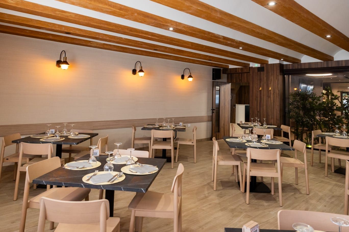 Comedor vacío de un restaurante con vigas de madera, lámparas colgantes y mesas y sillas cuidadosamente dispuestas.