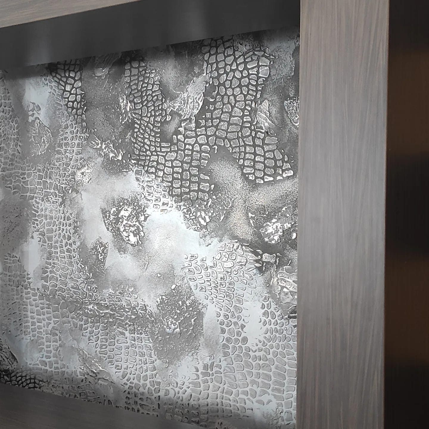 Arte de pared con textura plateada enmarcado en madera clara.