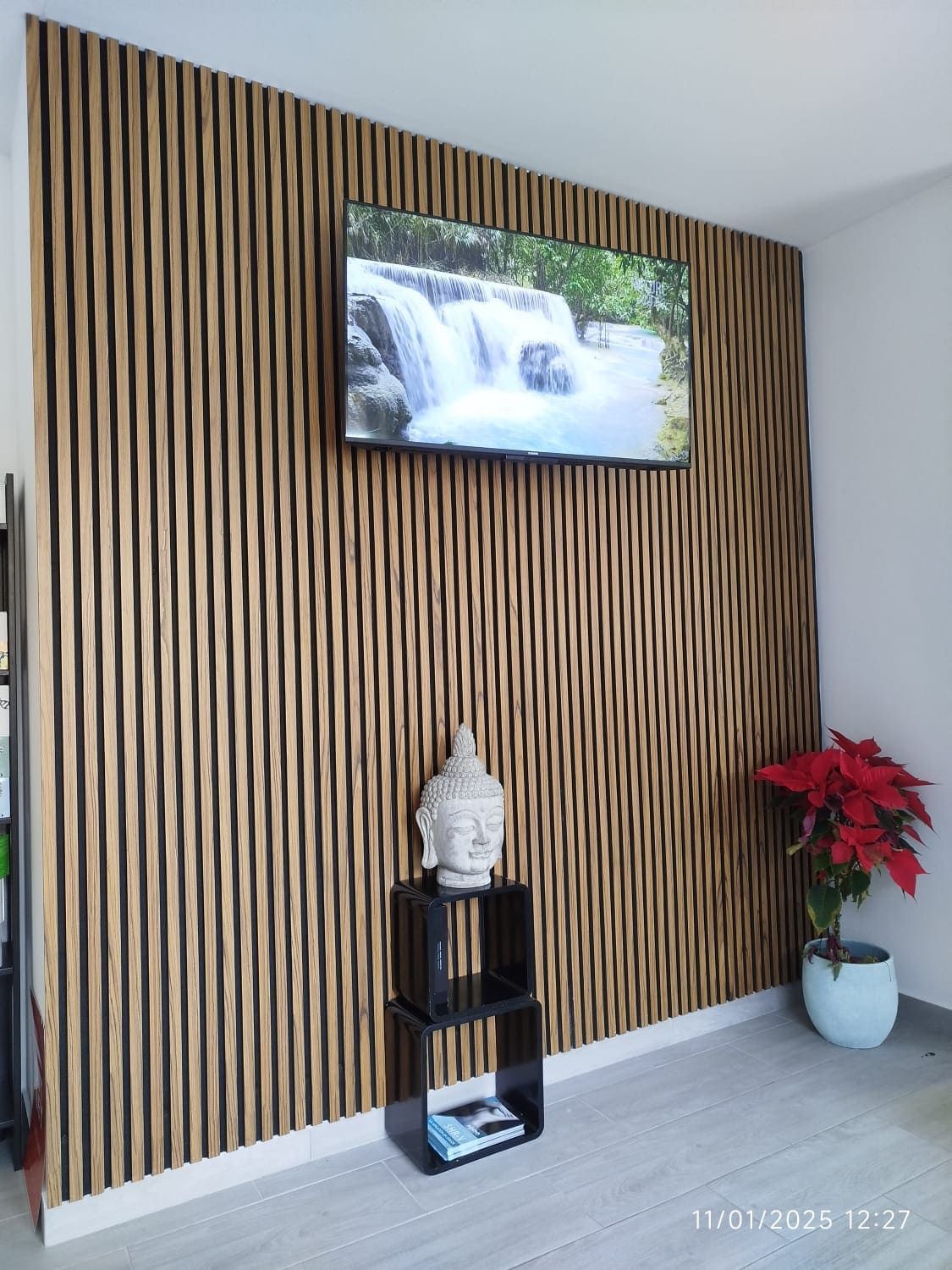Una pared con acento de listones de madera con un televisor montado, una estatua de Buda y una flor de Pascua en maceta.