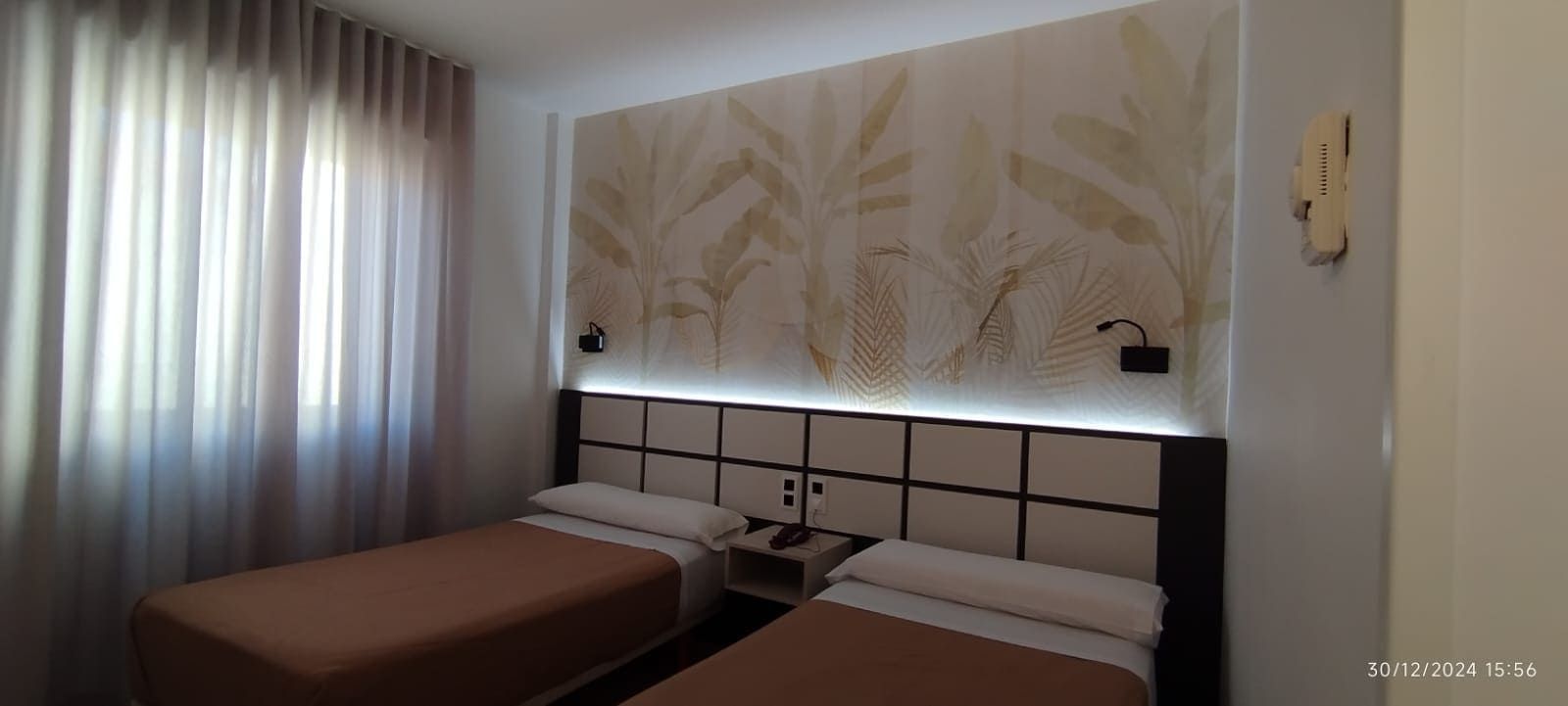 Camas individuales en una moderna habitación de hotel con cabecero decorativo y arte floral en la pared.