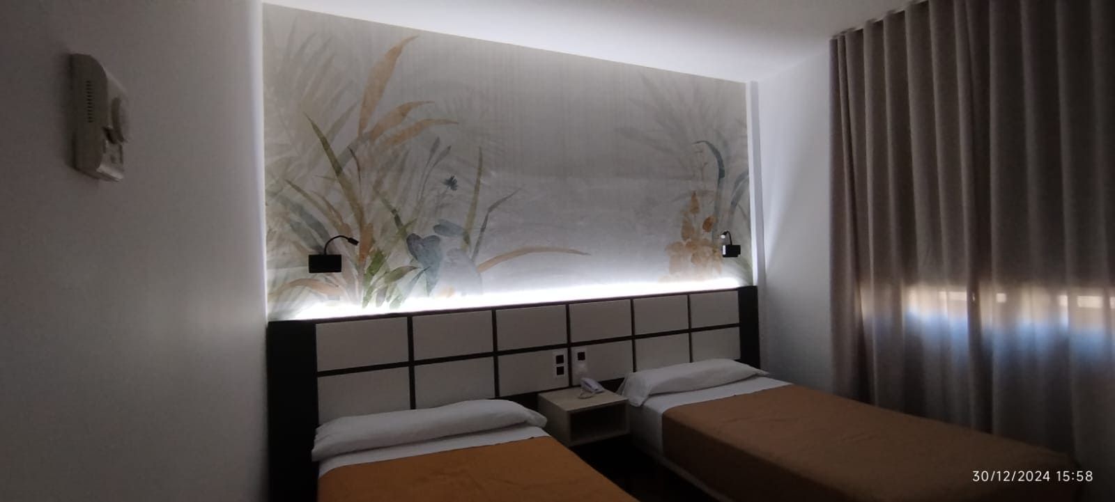 Camas individuales en una moderna habitación de hotel con arte decorativo en la pared y cortinas en tonos neutros.