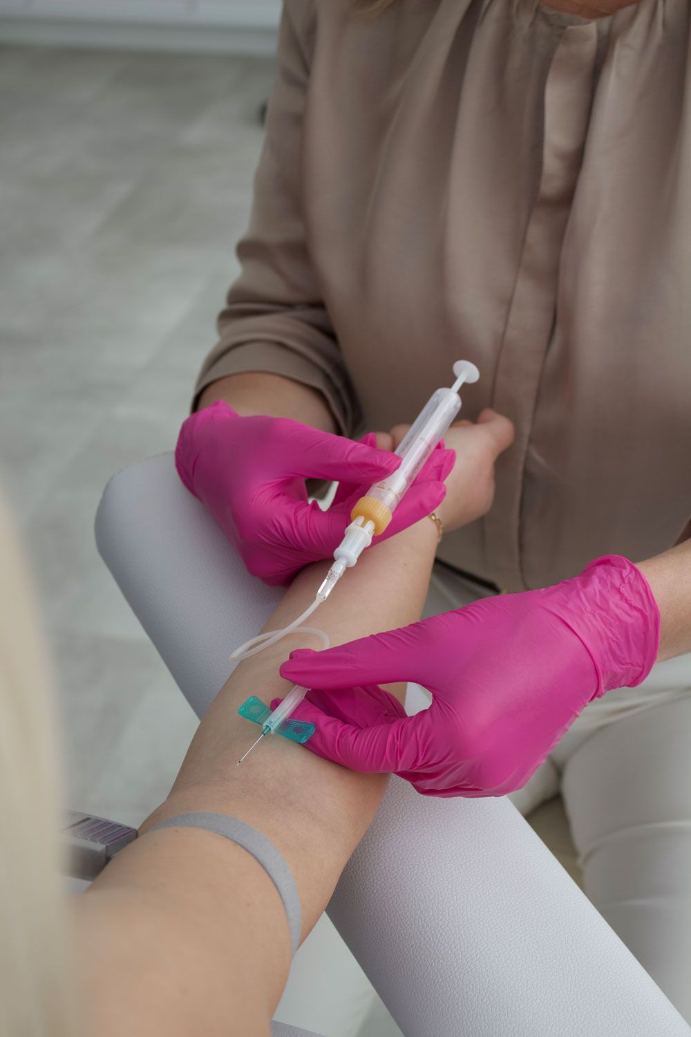 Eine Frau mit rosa Handschuhen bekommt eine Spritze in den Arm.