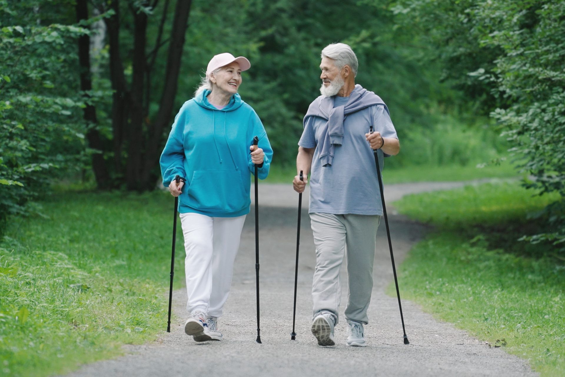 Ein Mann und eine Frau gehen mit Walking-Stöcken in einem Park spazieren.
