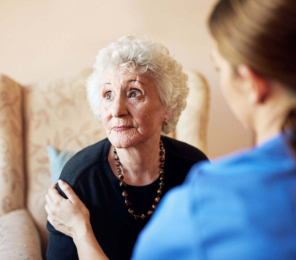 Eine ältere Frau sitzt auf einem Stuhl und spricht mit einer Krankenschwester.