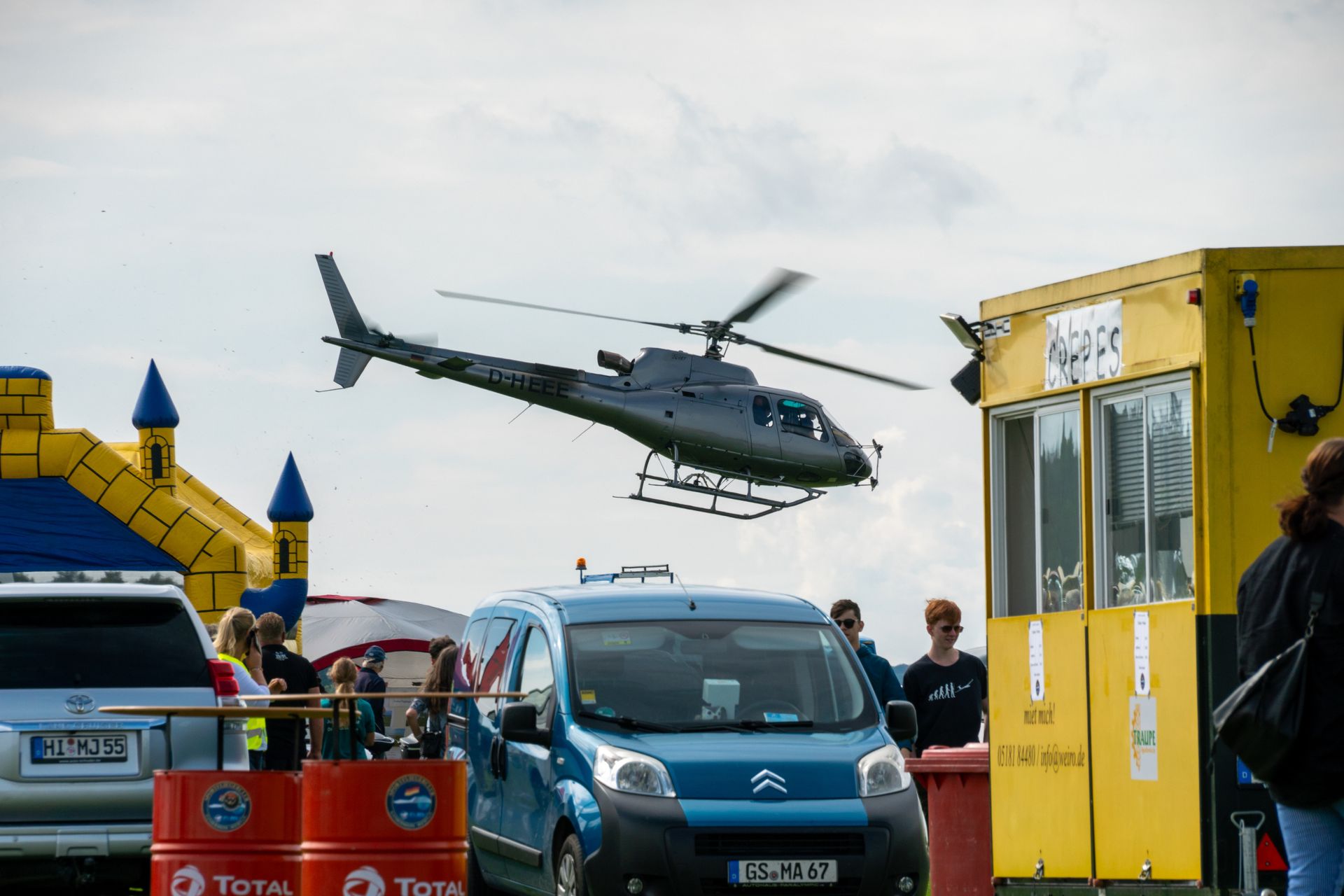Ein Hubschrauber startet an einem bewölkten Tag in der Nähe eines blauen Lieferwagens und eines gelben Standes.