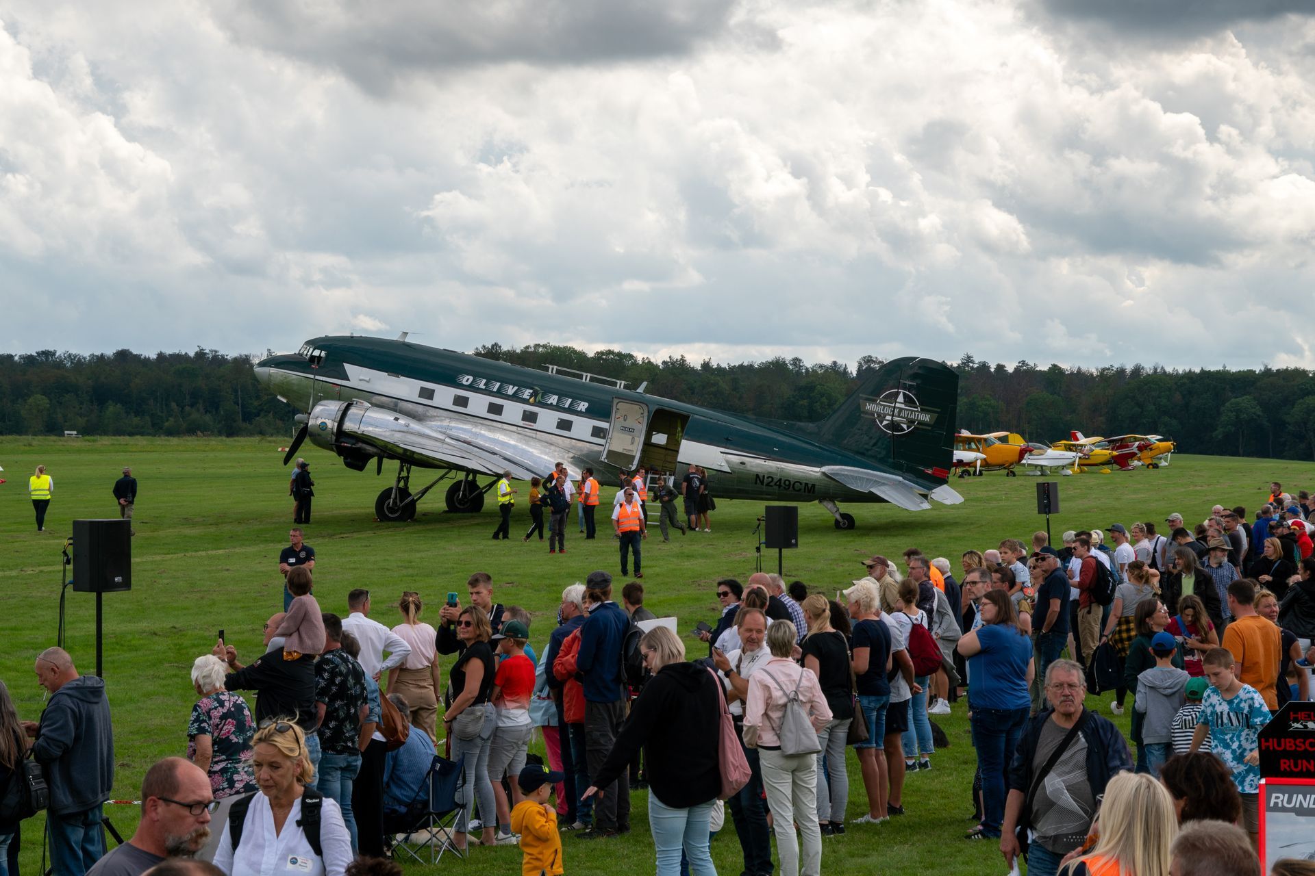 Eine große Menschenmenge hatte sich in der Nähe eines geparkten Oldtimer-Flugzeugs auf einem grasbewachsenen Feld versammelt. Die Leute standen da, schauten zu, und einige stiegen in das Flugzeug ein.