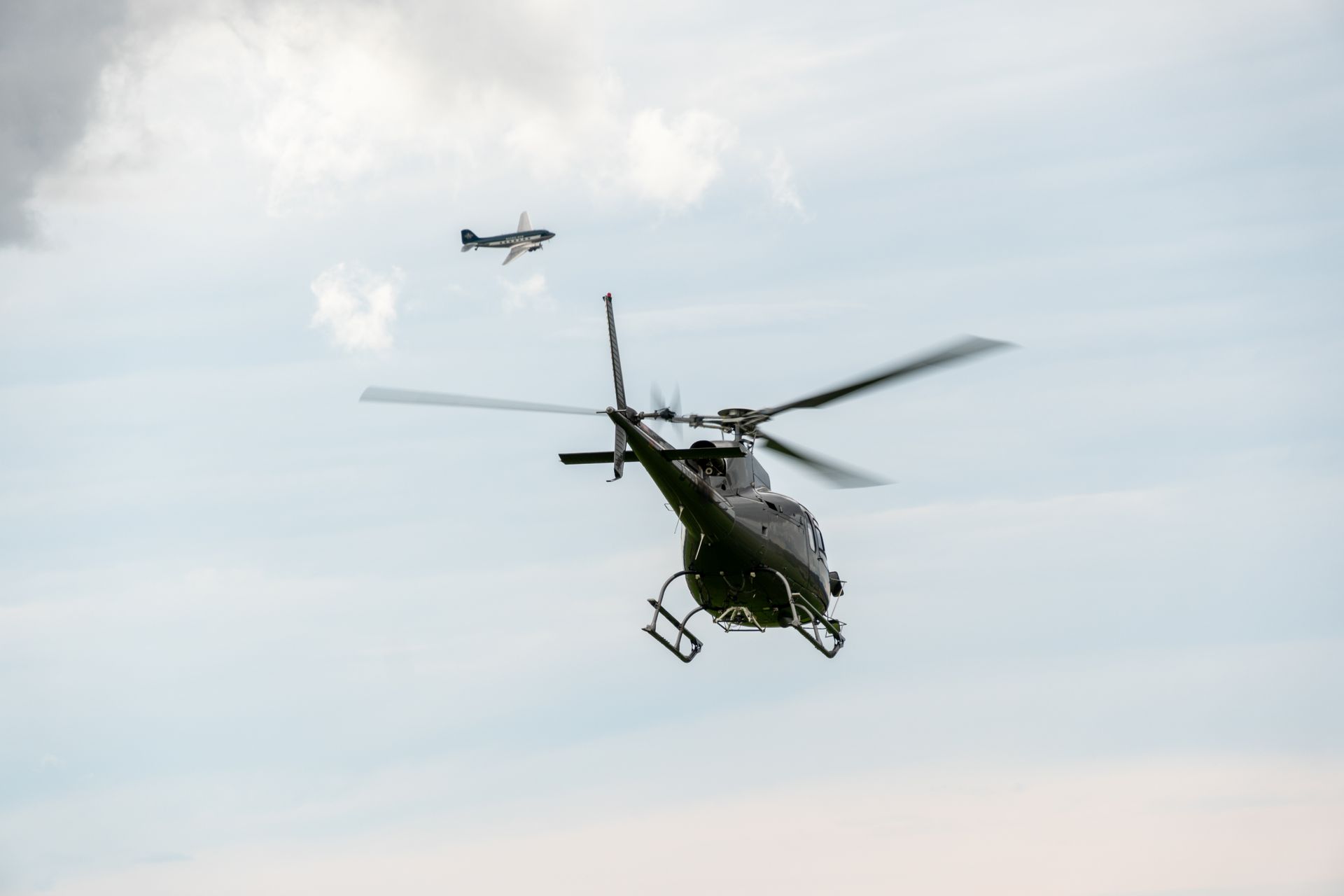 Hubschrauber und Kleinflugzeug fliegen in einem bewölkten Himmel.