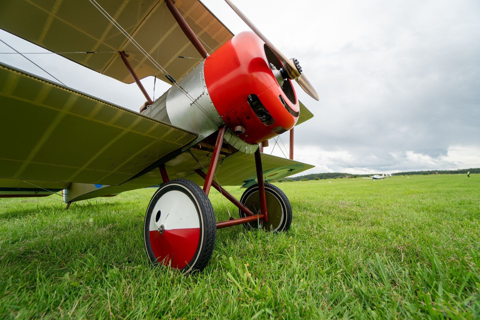 Ein rot-silbernes Doppeldeckerflugzeug auf einem grünen Grasfeld unter bewölktem Himmel.