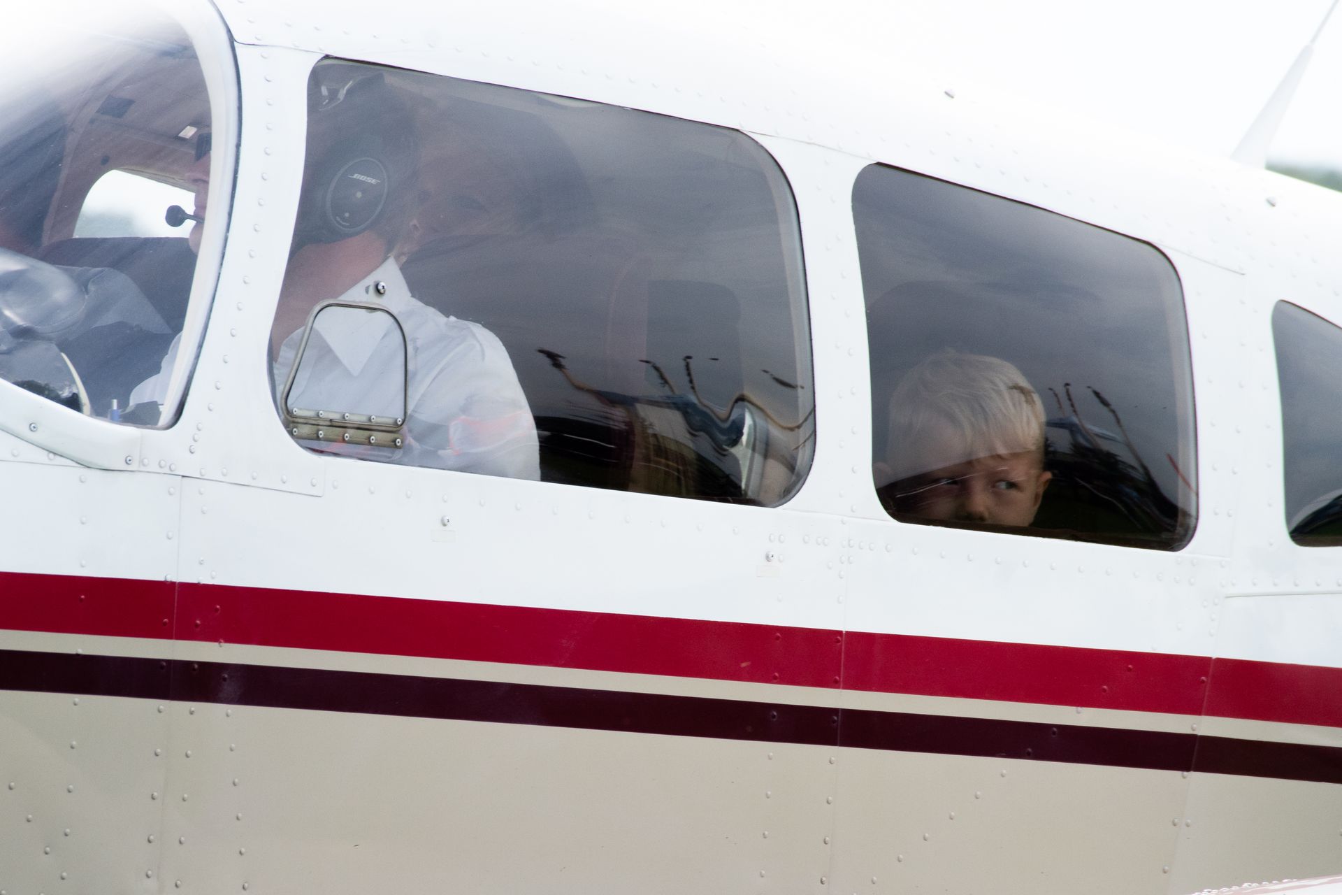 Zwei Personen in einem kleinen weißen Flugzeug. Roter Streifen an der Seite.