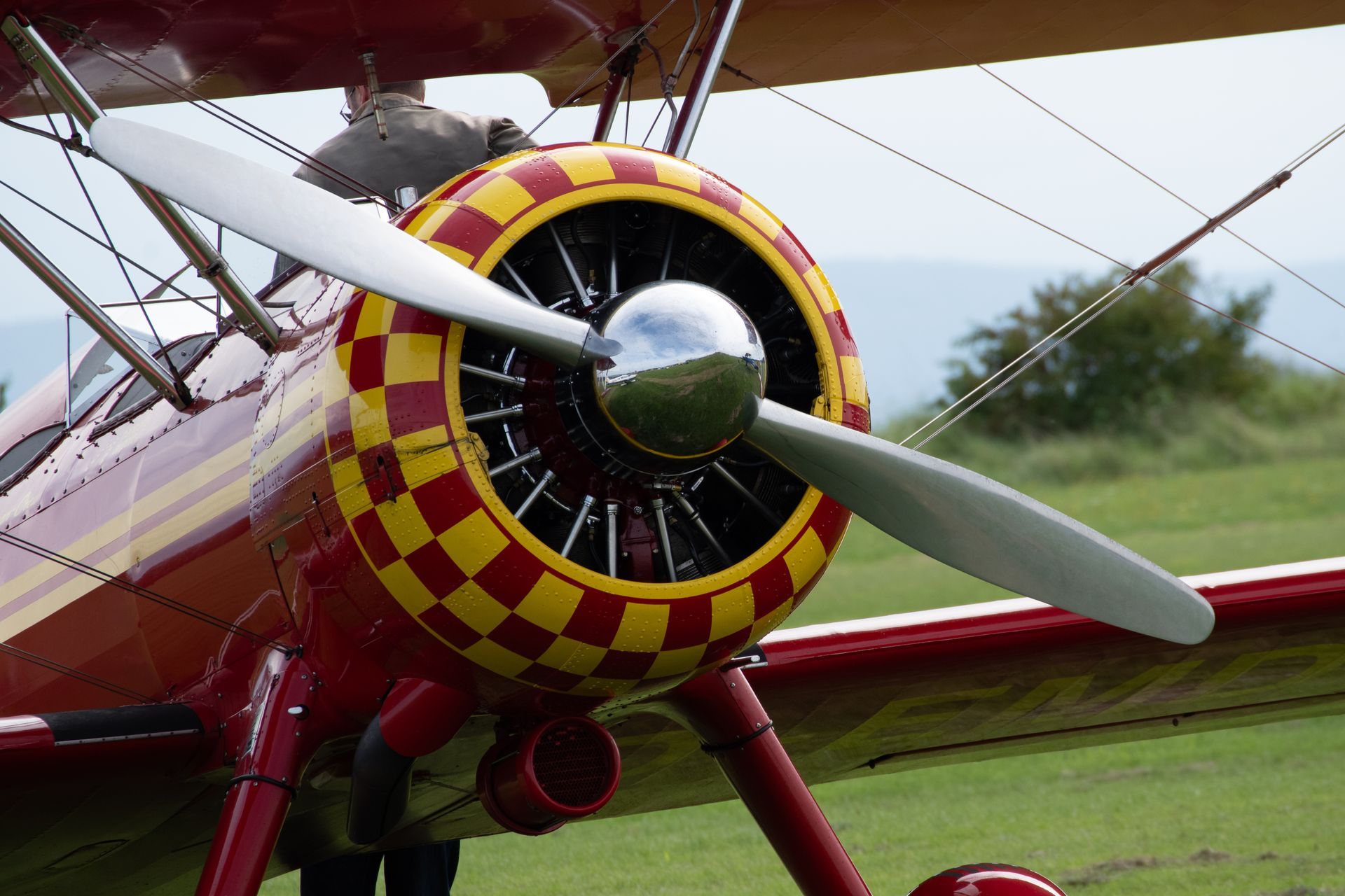 Rotes Doppeldeckerflugzeug mit schachbrettartiger Motorverkleidung und drehbarem Propeller.