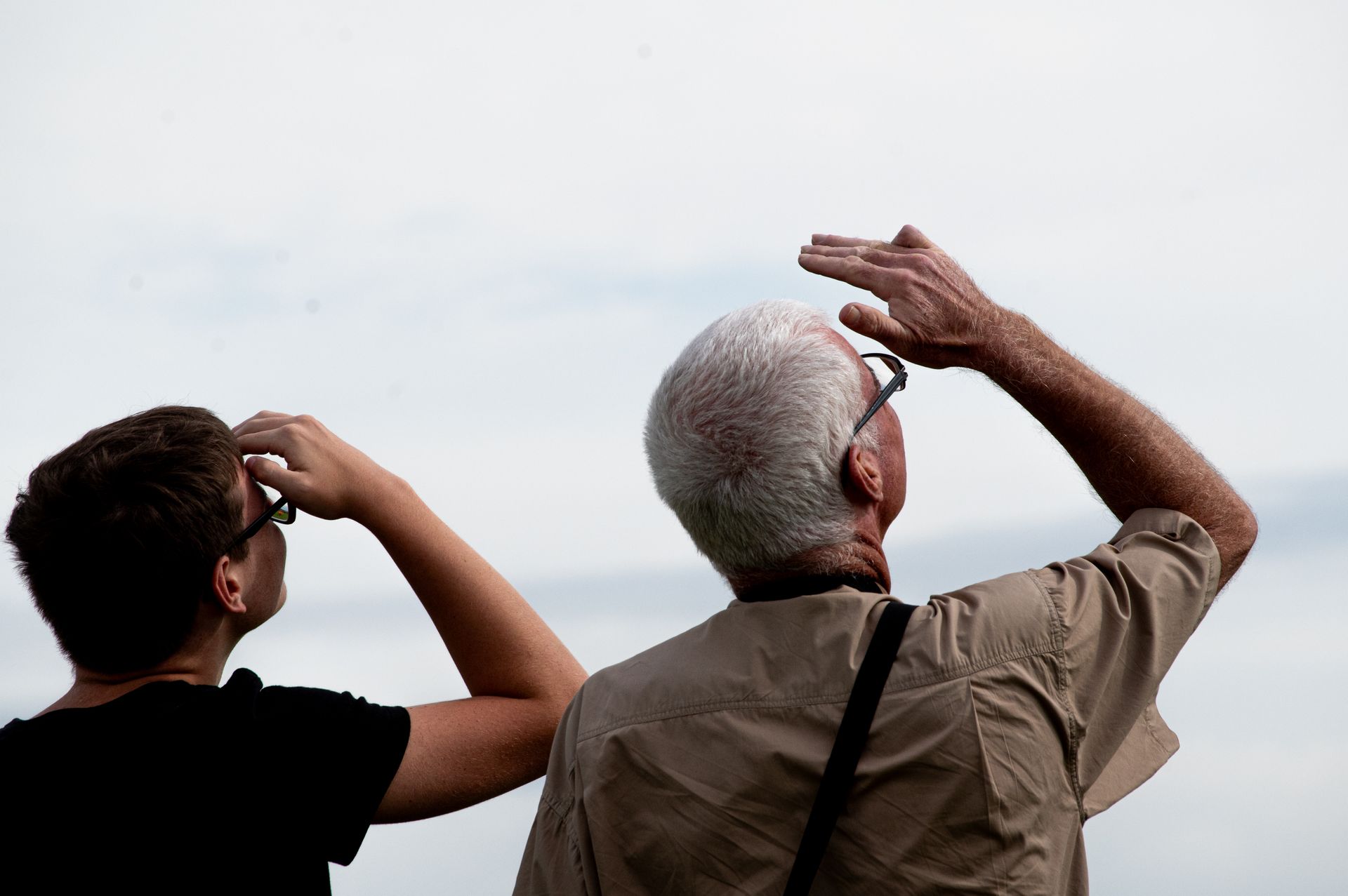 Zwei Personen blicken nach oben und schützen ihre Augen. Bewölkter Himmel.