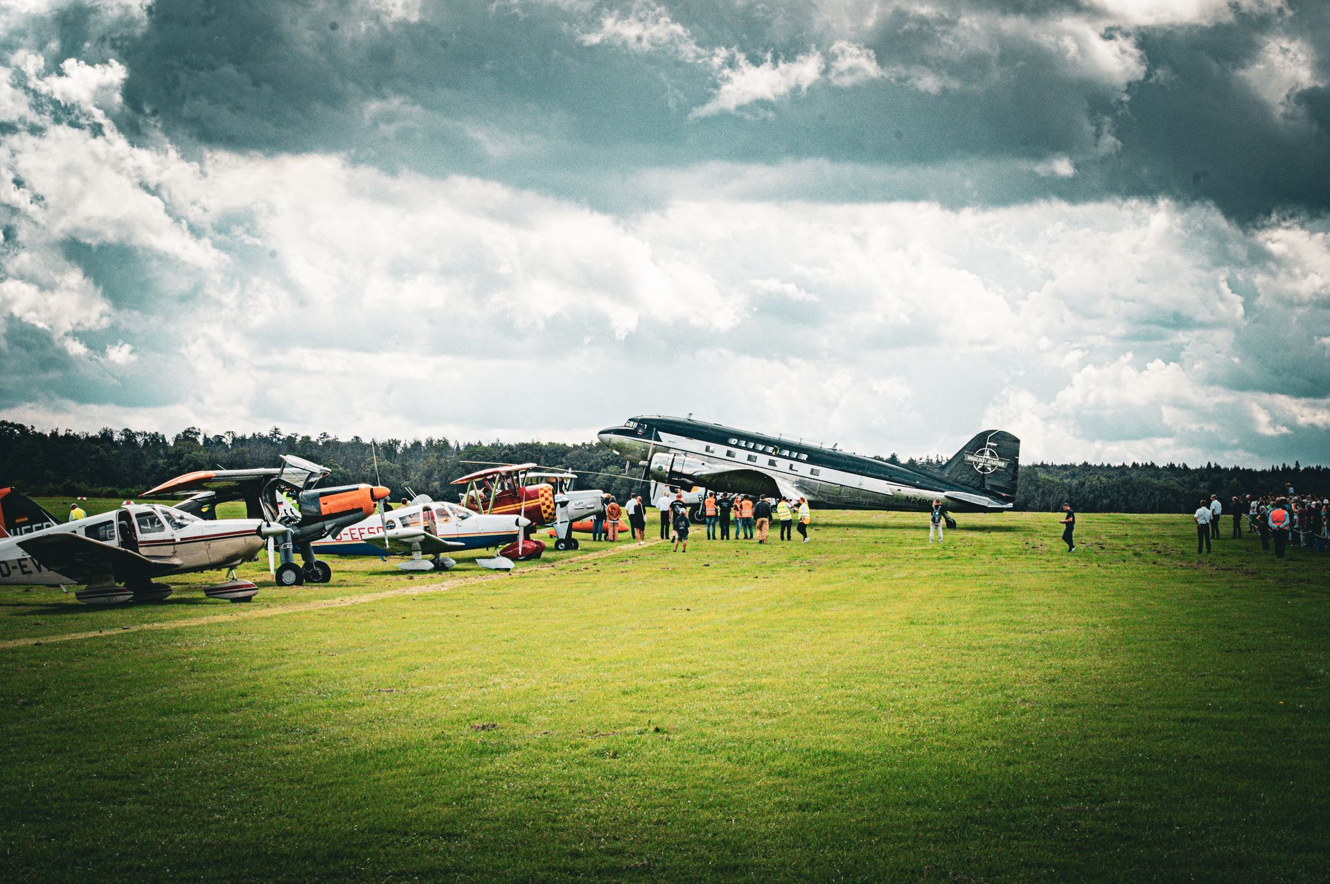 Flugzeuge parkten auf einem grasbewachsenen Feld, um das sich unter bewölktem Himmel Menschen drängten.