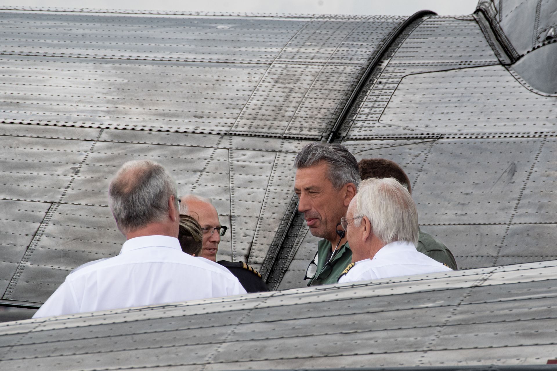 Männer in Hemden und Uniformjacken unterhalten sich in der Nähe eines Flugzeugflügels aus Metall.