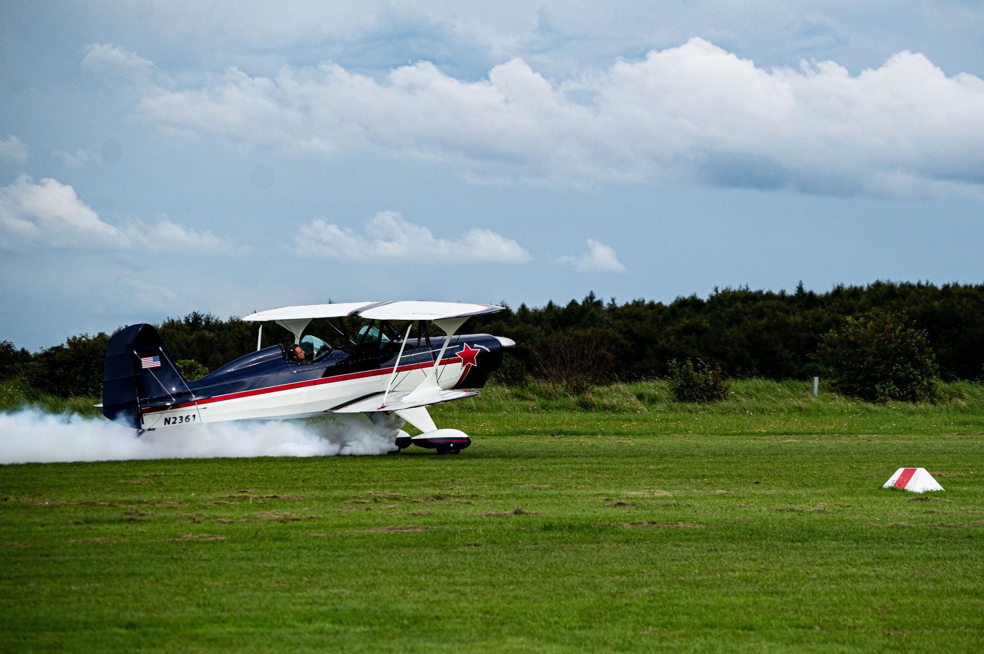 Ein Doppeldecker landet auf einem grasbewachsenen Feld und wirbelt eine weiße Staubwolke auf.