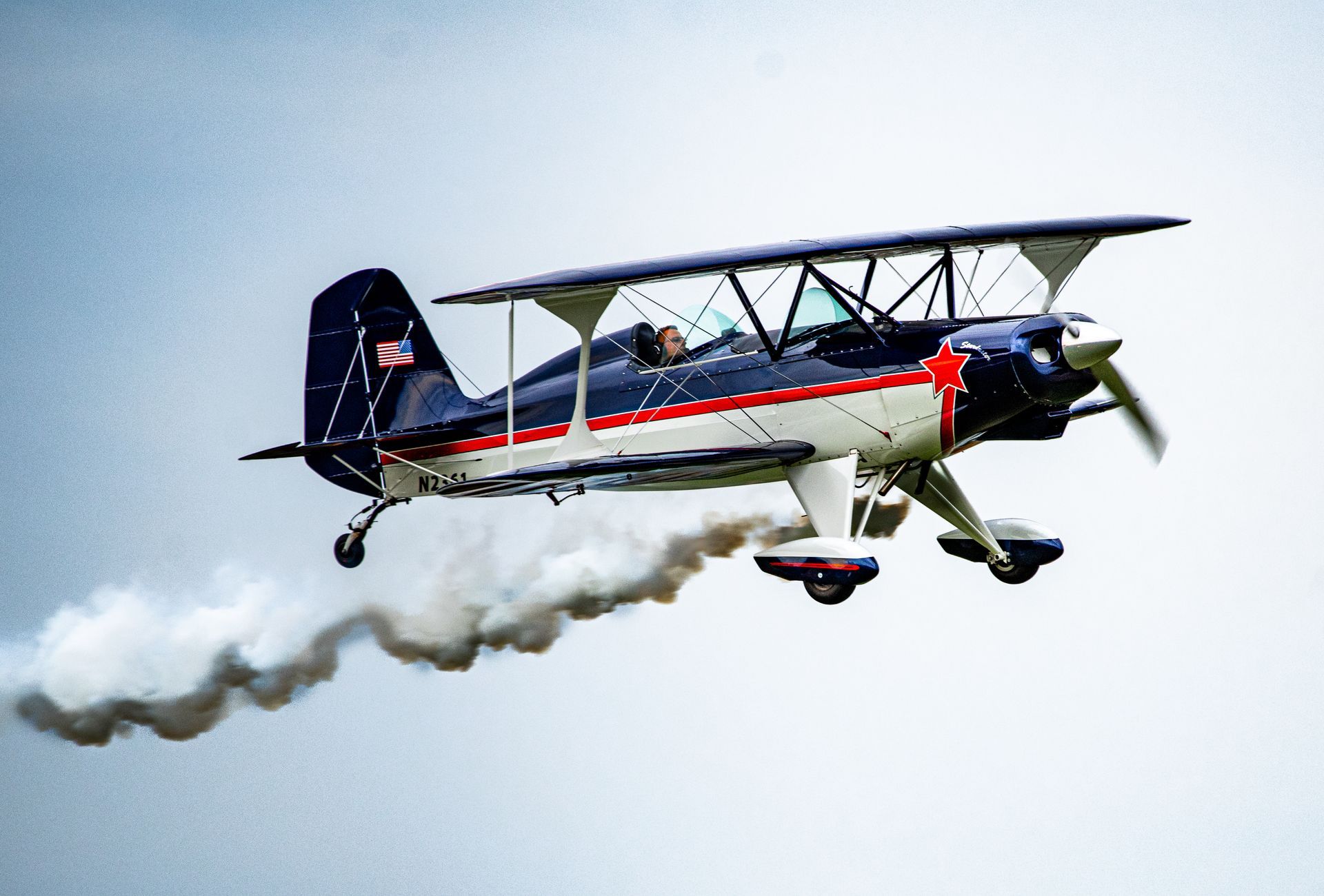 Doppeldecker im Flug, der eine Rauchspur ausstößt, marineblau und weiß mit roten Streifen.
