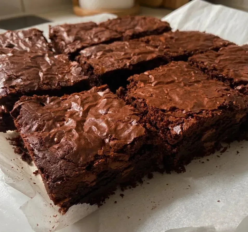 Brownies de chocolate recién horneados sobre papel de horno, cortados en cuadrados y con la superficie agrietada.