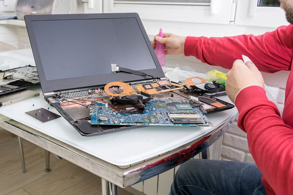 Un hombre está arreglando una computadora portátil en una mesa.