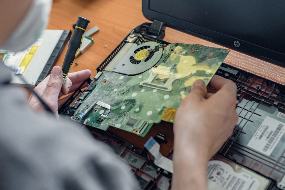 Un hombre que lleva una máscara está arreglando una computadora portátil.