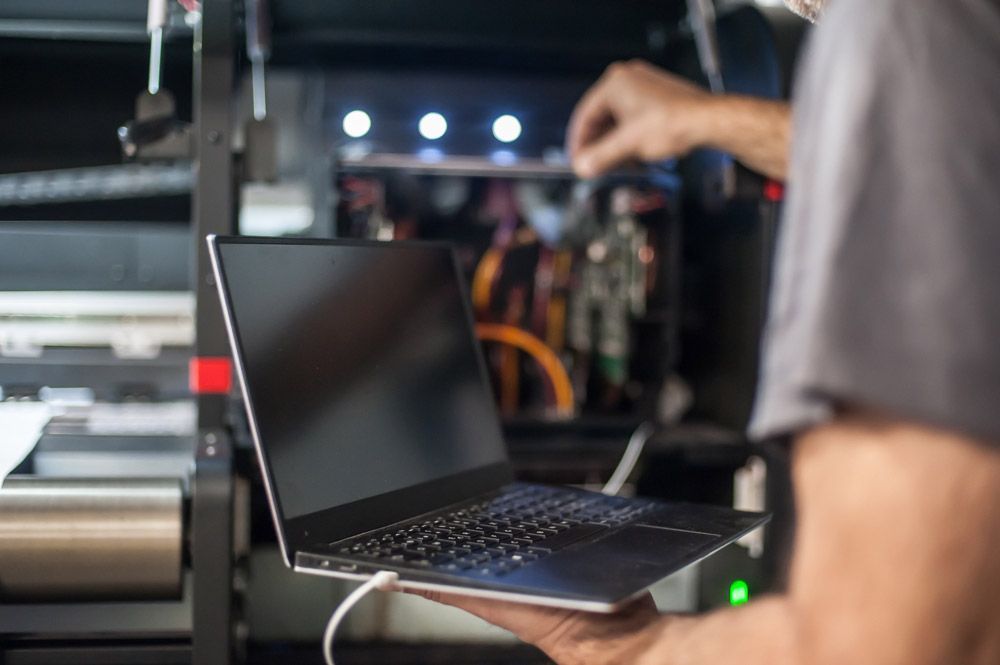 Un hombre sostiene una computadora portátil en sus manos frente a una impresora.