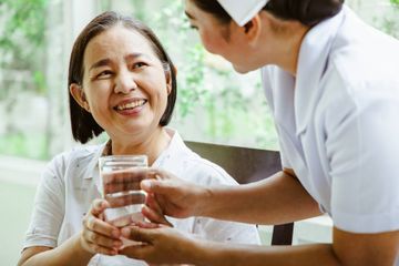 Pflegerin reicht einer älteren Frau einen Tee