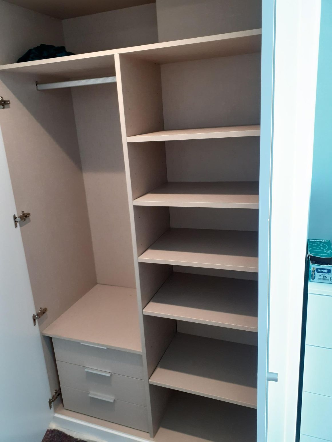 Armario abierto beige con baldas y barra para colgar.