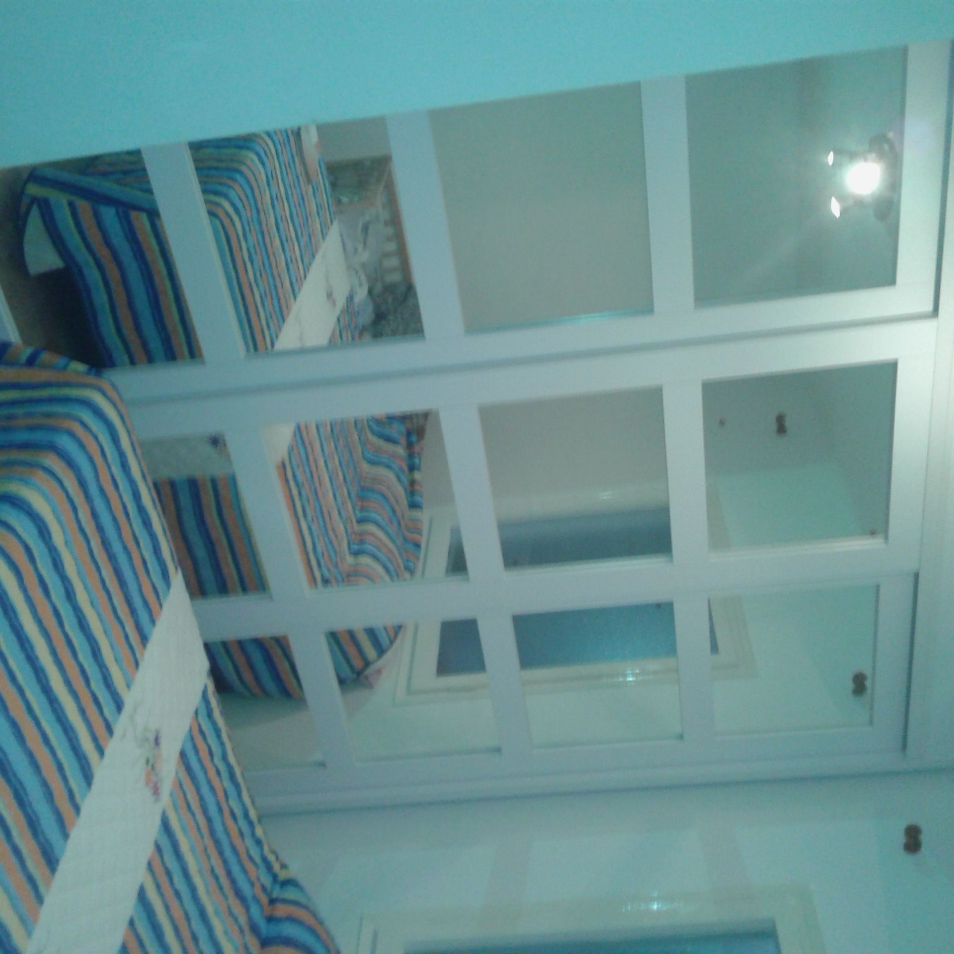 Las puertas de armario con espejo reflejan un dormitorio con ropa de cama a rayas y paredes azules.