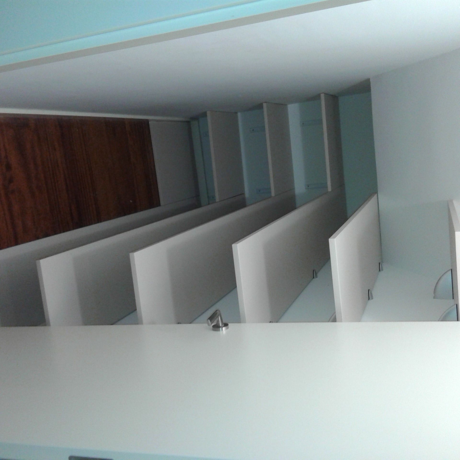 Cubículos de oficina blancos con una pared trasera de madera, vistos desde un ángulo bajo.