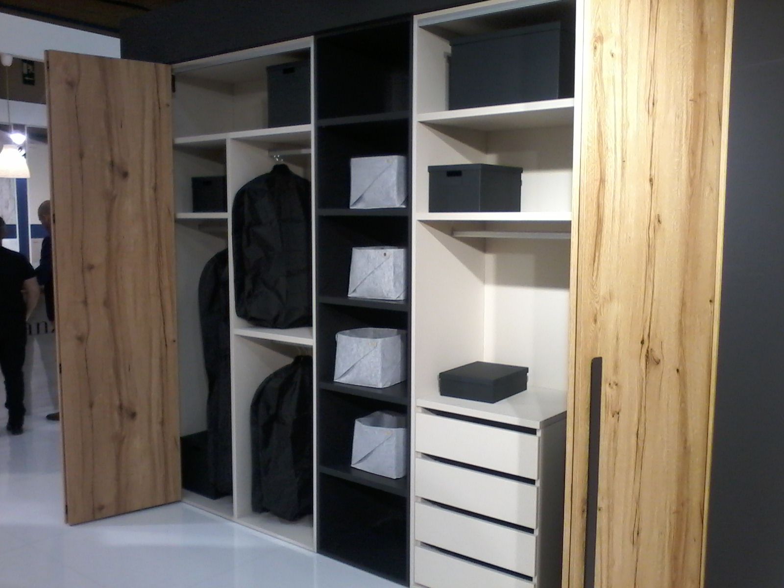 Armario de madera con puertas abiertas, estantes en blanco y negro, ropa y cajas de almacenaje.