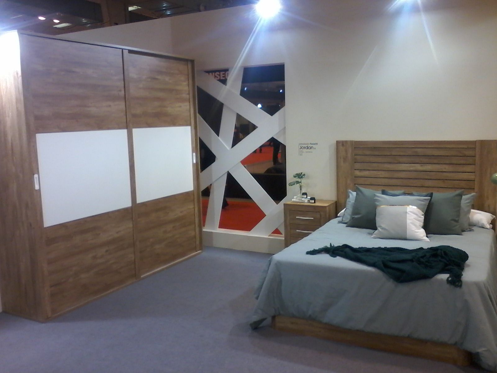 Recámara con muebles de madera: closet con puertas corredizas, cama con almohadas y mesita de noche.