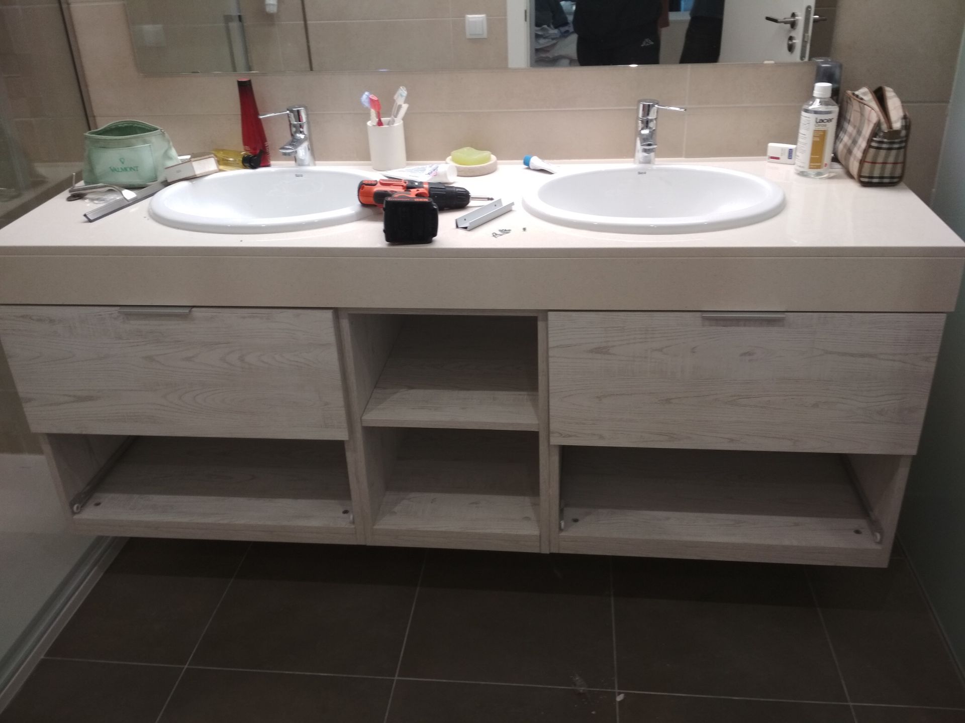 Mueble de baño con dos lavabos, cajones y estantes, con herramientas y artículos de tocador sobre encimera.