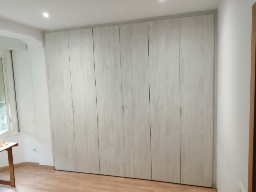 Armario grande de madera de color claro con múltiples puertas, empotrado en la pared de una habitación.