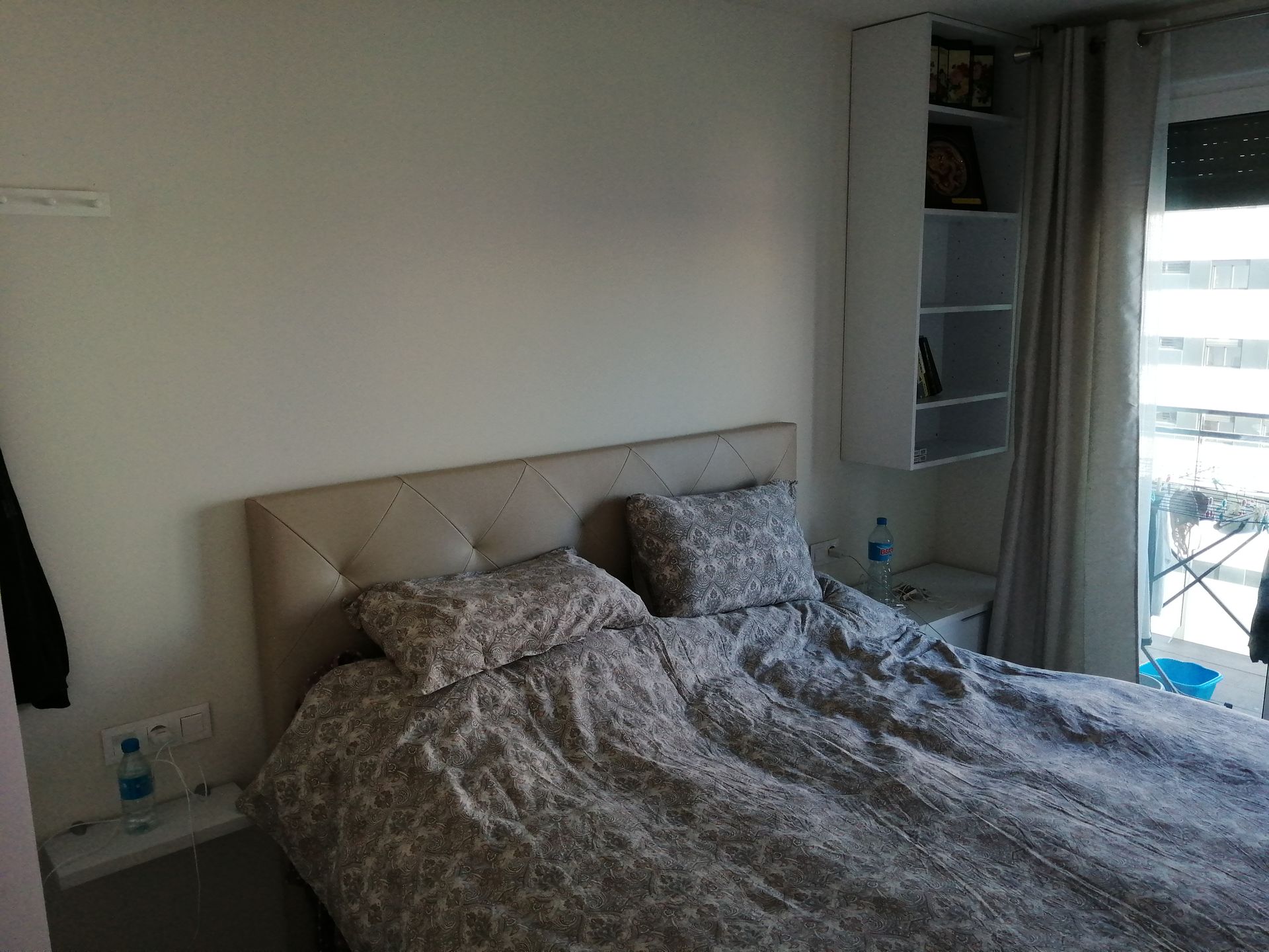 Dormitorio con cabecero capitoné beige, ropa de cama estampada y estantes blancos.