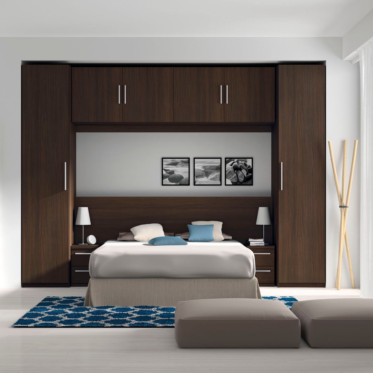 Juego de dormitorio con gabinetes de madera oscura que enmarcan una cama, alfombra azul y otomanas neutrales.