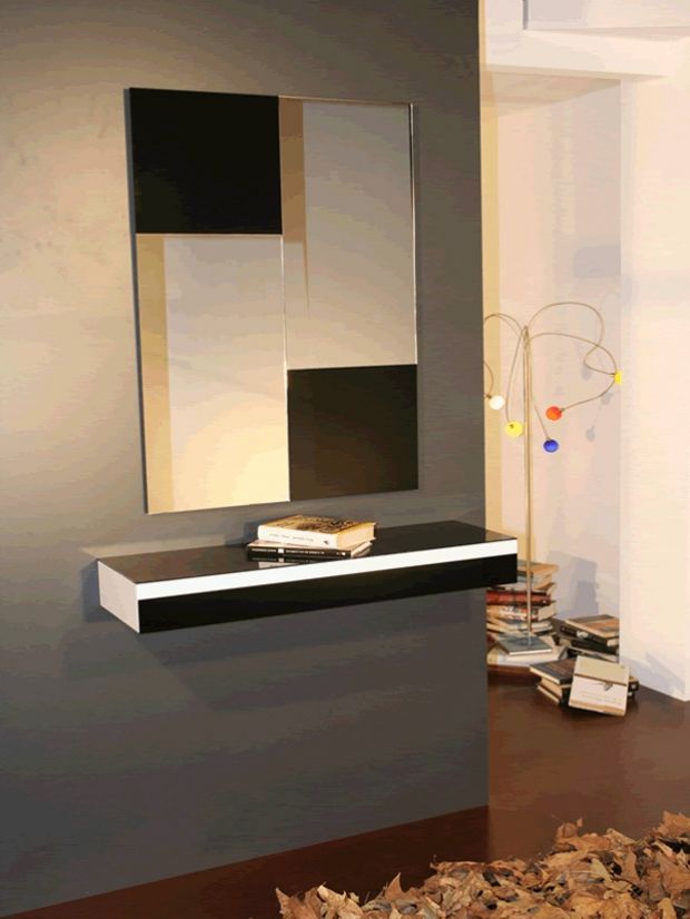 Espejo geométrico sobre un estante blanco y negro con libros, contra una pared gris.