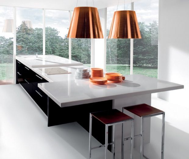 Cocina moderna con isla de encimera blanca, gabinetes negros, luces colgantes de cobre, taburetes y platos.