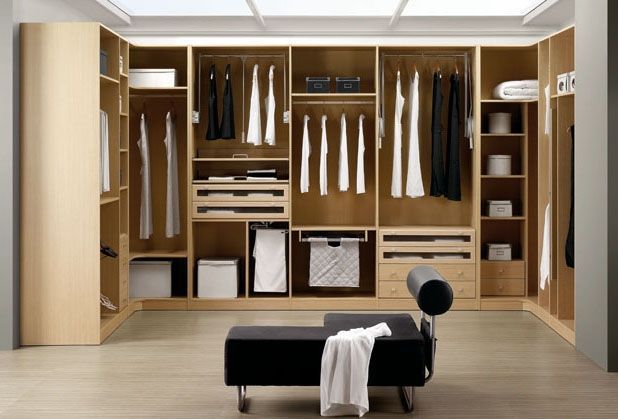 Vestidor con estanterías de madera clara, tendedero, cajones y banco con toalla.