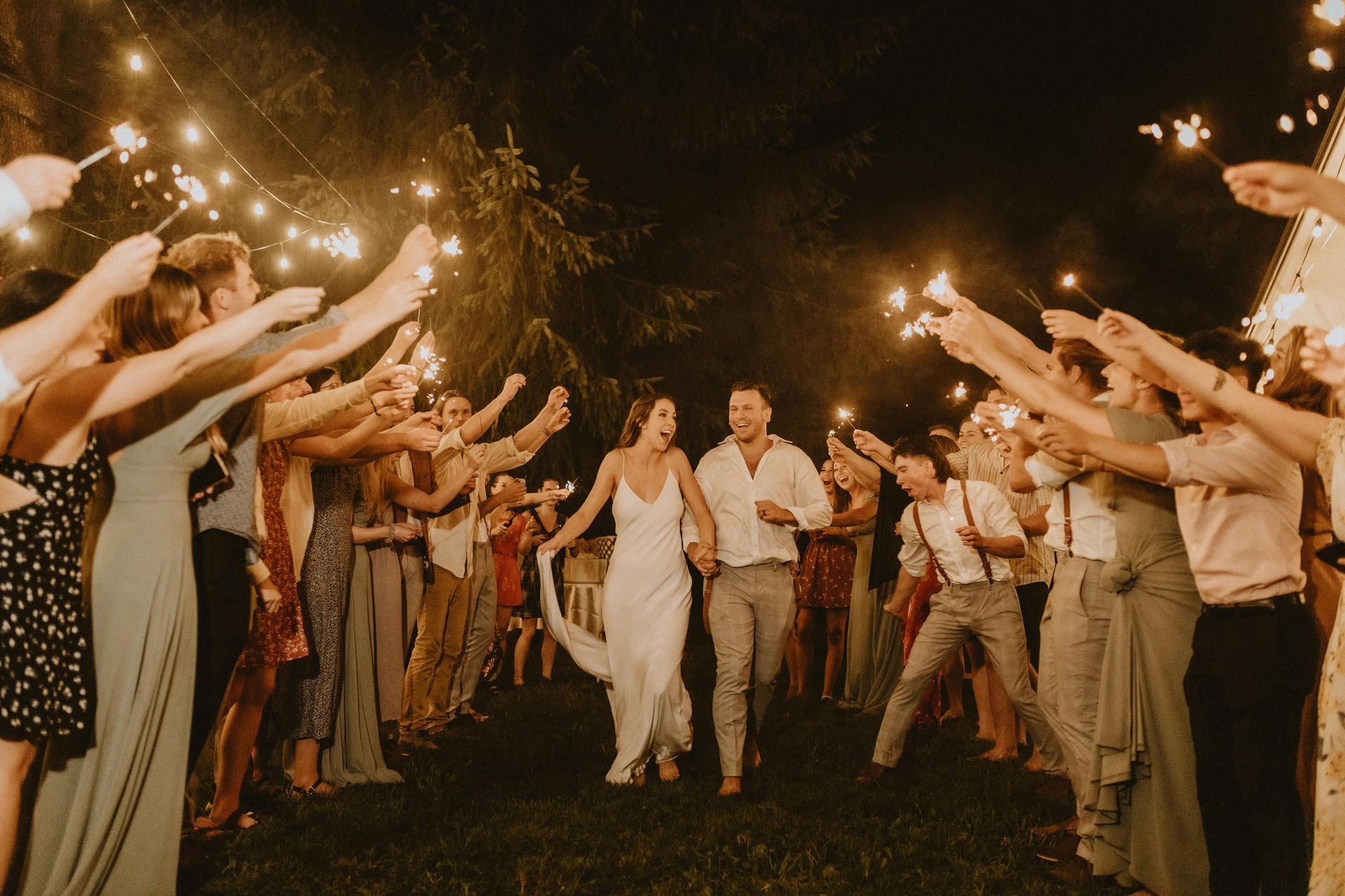 Una novia y un novio caminan a través de un túnel de bengalas en la recepción de su boda.