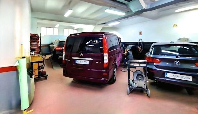 Una furgoneta y un coche en un taller. Una persona trabaja en la furgoneta.