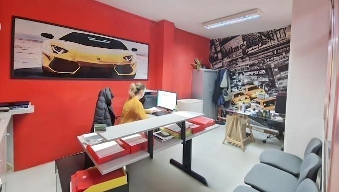 Mujer en un escritorio en una oficina con temática de automóviles, paredes rojas, arte de automóviles