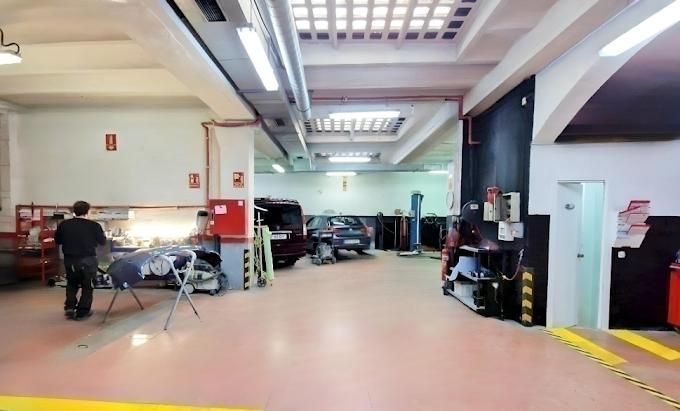 Dentro de un taller de reparación de automóviles: un mecánico trabaja en un coche, suelo rojo, herramientas, vehículos