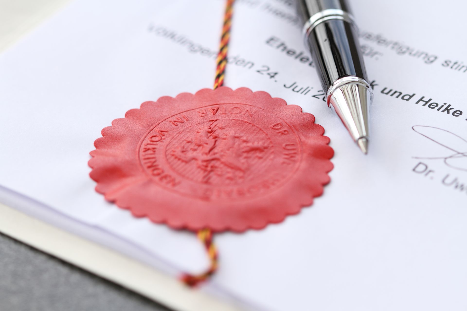 Auf einem Blatt Papier befinden sich ein rotes Siegel und ein Stift.