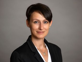 Eine Frau in schwarzer Jacke und weißem Hemd lächelt in die Kamera.