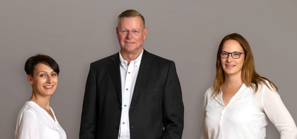 Ein Mann im Anzug und zwei Frauen in weißen Hemden stehen nebeneinander.