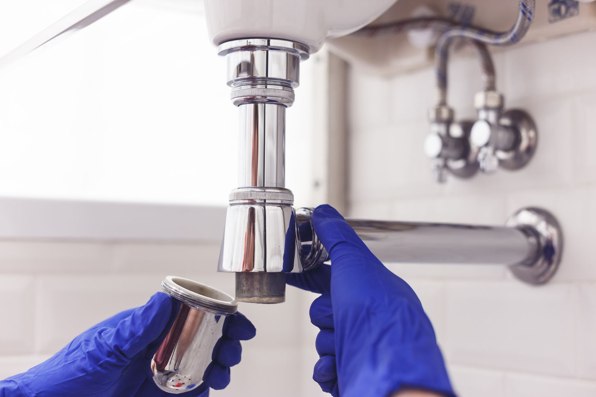 Plombier débouchant un lavabo en dévissant le siphon.